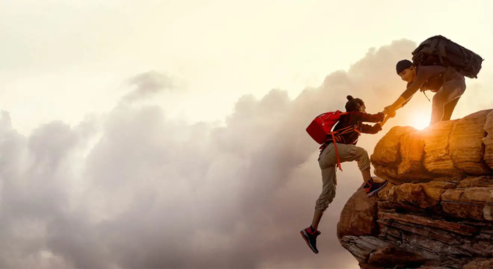 A hiker pulling up another on top of a cliff