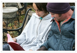 A young man and woman sitting on a bench reading the Bible