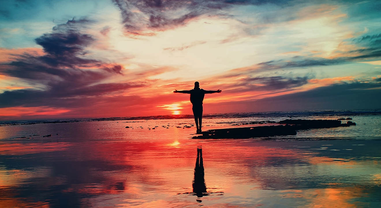 A person standing with their arms outstretched on a beach