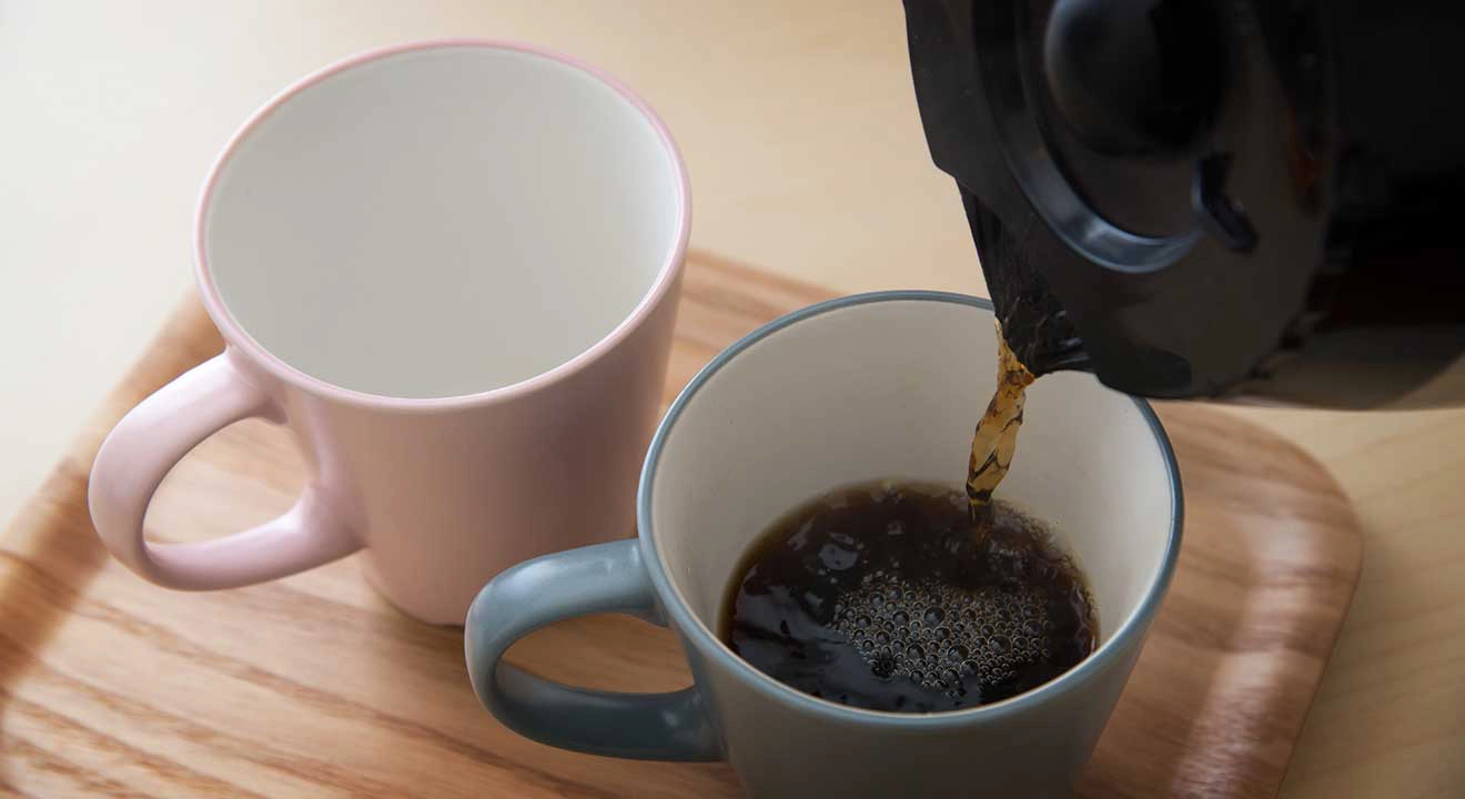 Coffee pouring into one of two cups on a tray