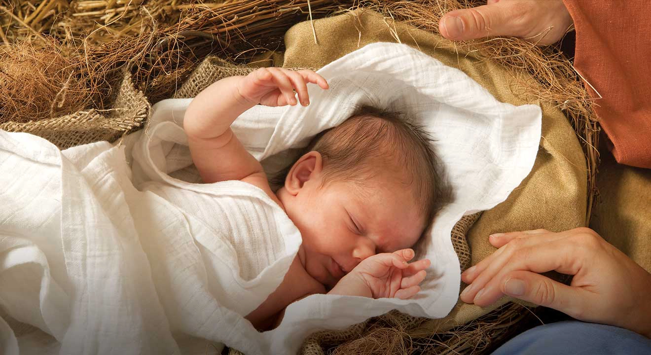 An infant in swaddling clothes in the hay