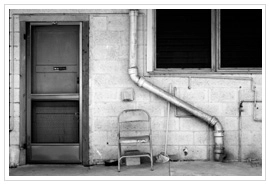 An old back door to a cinder block house with a metal chair