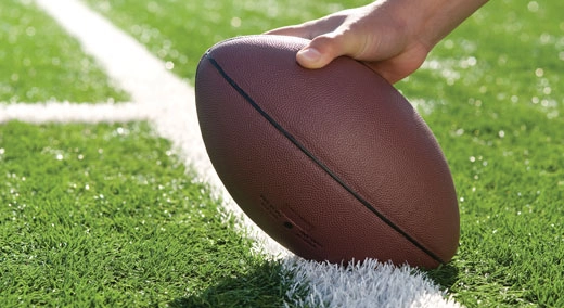 Right hand holding a football on a white line on a field
