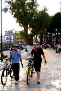 Two boys walking their bikes on a sidewalk