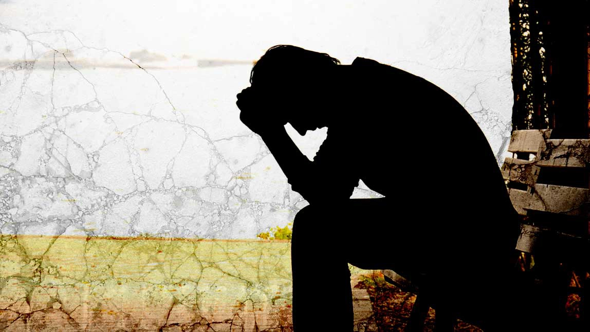 Silhouette of a man leaning his head on his hands while sitting on a park bench