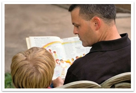 A father reading to his son sitting on a bench
