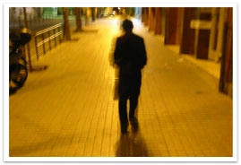 Shadowy figure of a man walking down a sidewalk at night