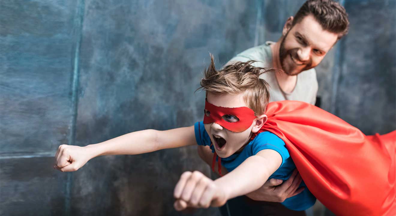 A father holding a son in a super hero suit