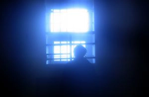 The silhouette of a person in a dark room looking out a bright window