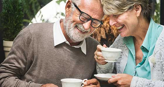 An elderly couple laughing over a cup of tea