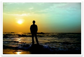 A young person standing in the water on the beach during sunset