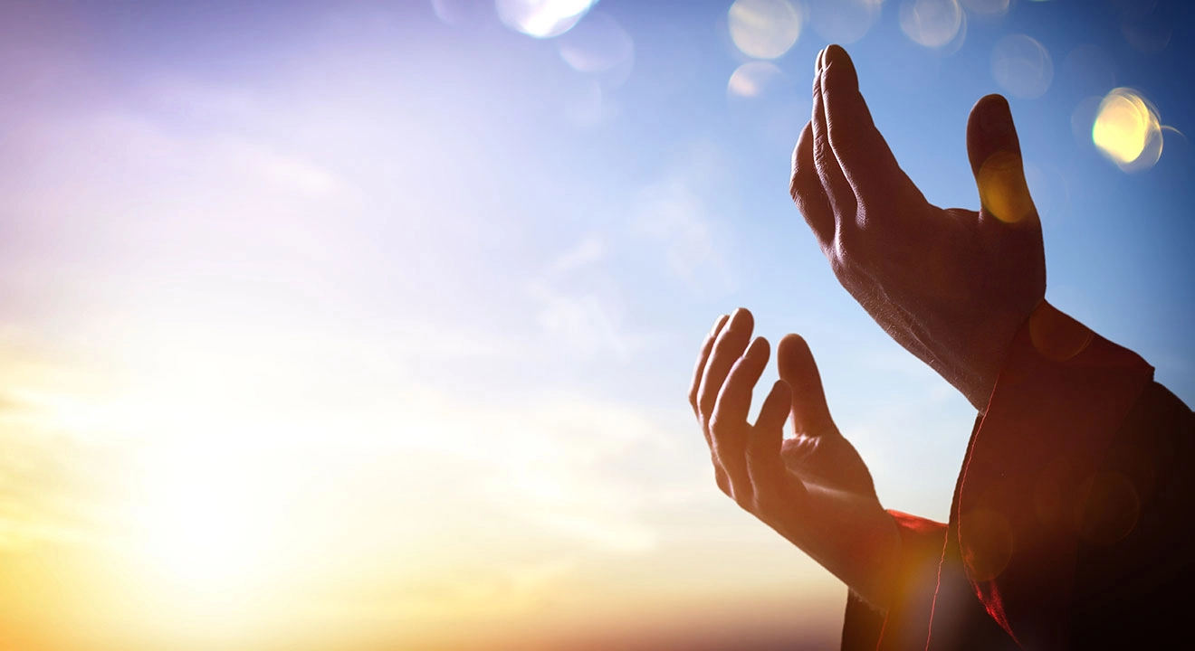 Open hands raised up in a blue sky and filtered sunshine