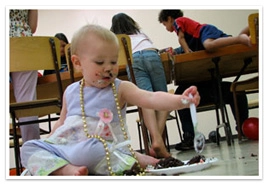 A baby eating chocolate cake while she sits on the floor