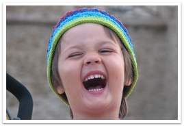 A young boy with a knit cap smiling closing his eyes