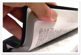 Close up of a left hand flipping through the pages of the Bible