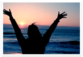 A woman with hands lifted high during sunset on an ocean