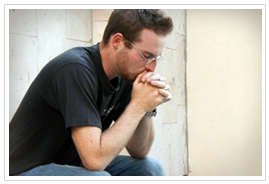 A man sitting praying with his hands folded over his mouth