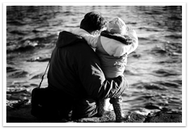 A father holding a child bundled up on the beach
