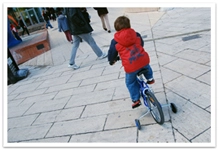 A child pedaling a bicycle with training wheels on a stone walkway
