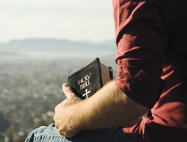 A man holding a bible while looking over a valley