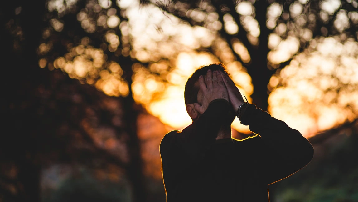 A man outside with his hands covering his face